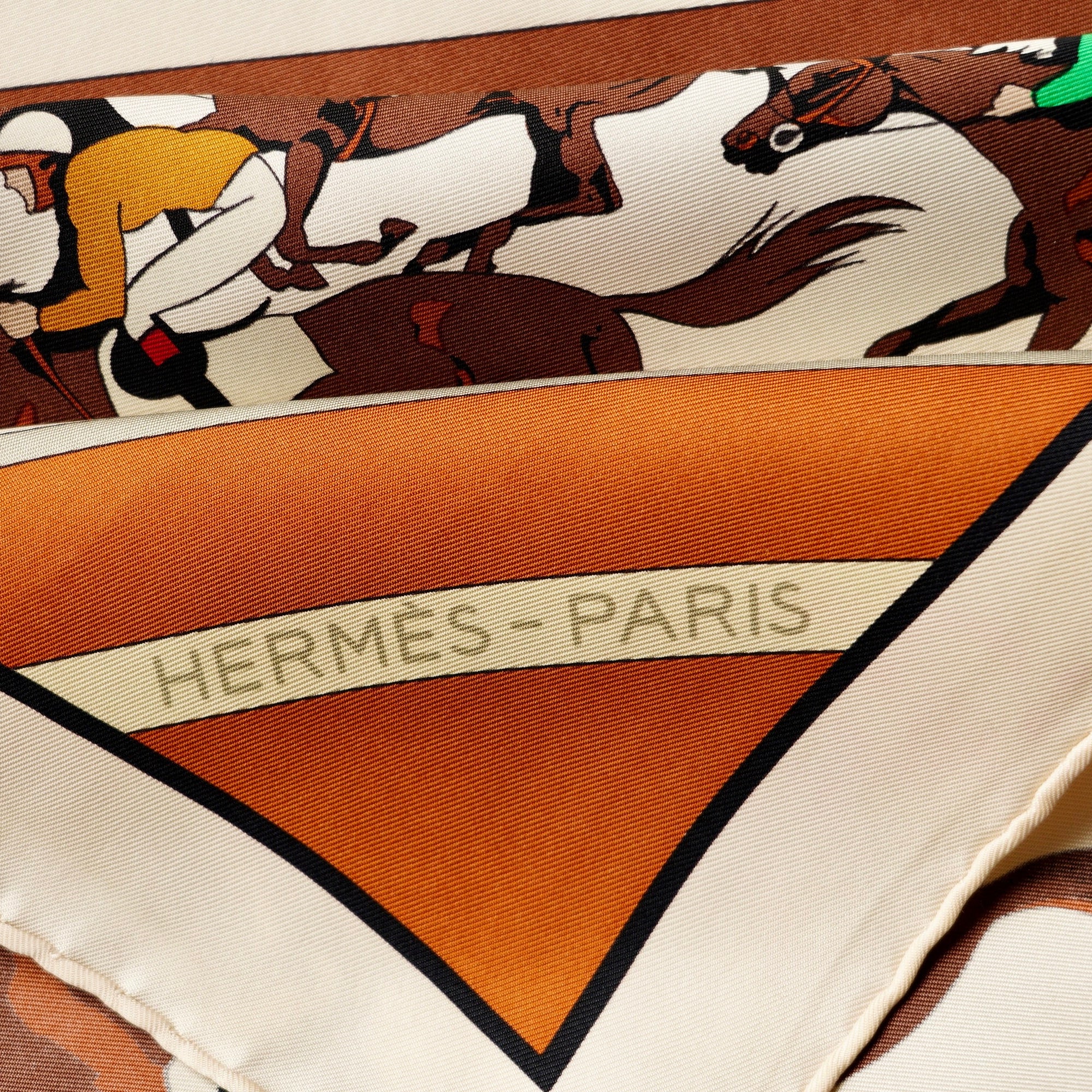 Gros plan sur le roulotté main du foulard Hermès "Les Courses" et un jockey en casaque verte.