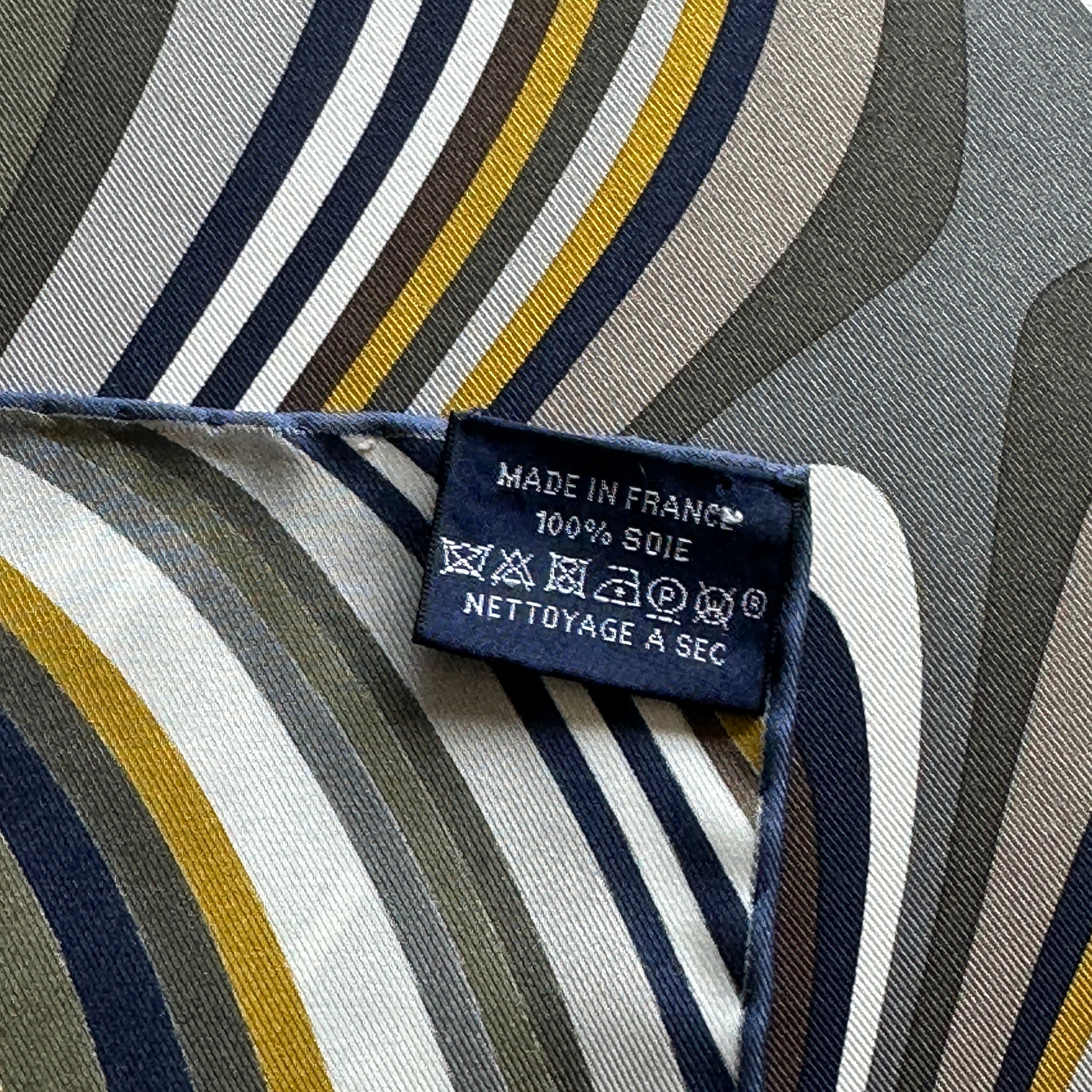 Zoom sur l'étiquette de composition "Made in France 100% Soie" cousue sur le bord roulotté bleu du foulard.